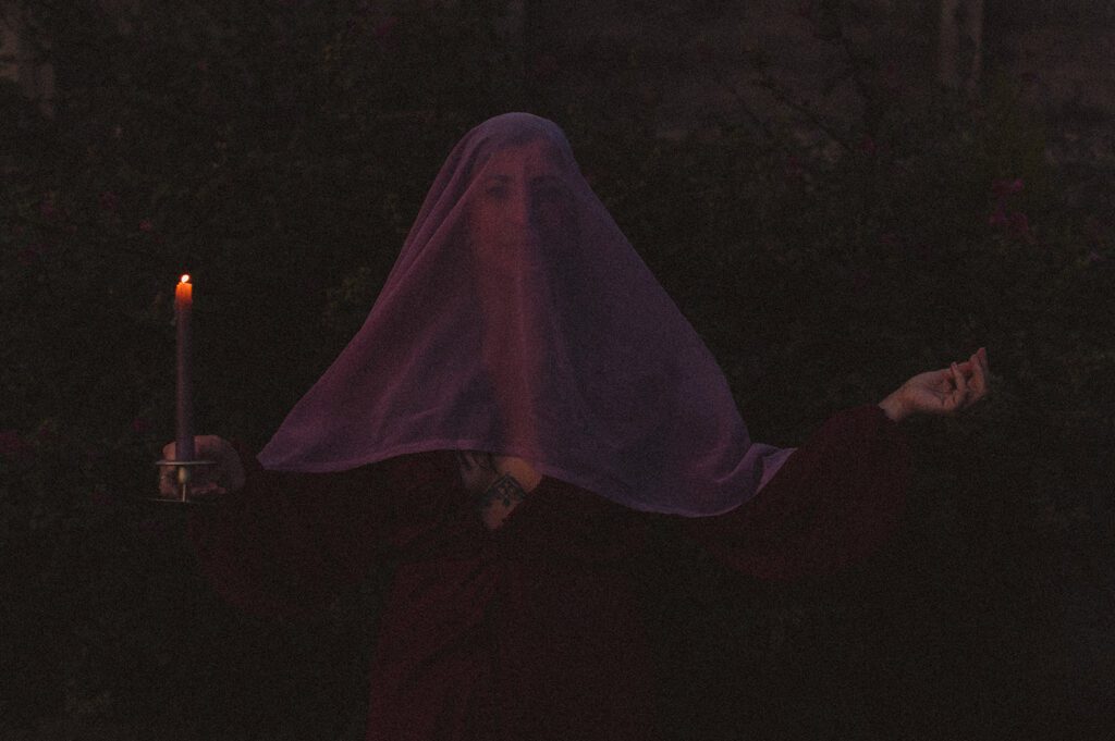 Miriam holding a candle wearing a veil over her face - dark feminine energy.