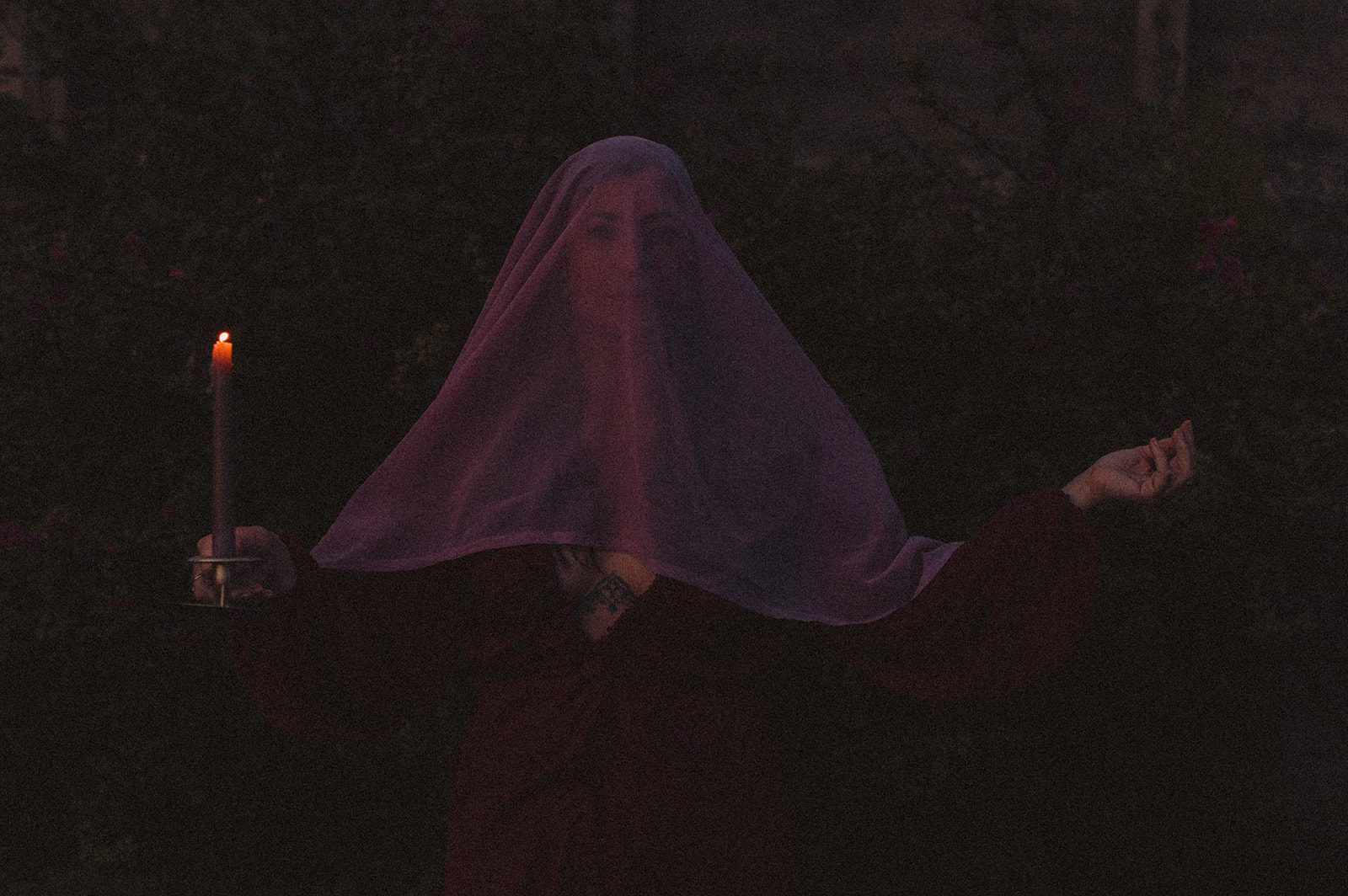 Miriam holding a candle wearing a veil over her face - dark feminine energy.